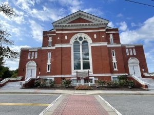A large red-brick building in Canton, GA with arched windows, white trim, and three white doors. A sign above the center door reads Public Safety and Canton Theatre. The sky is blue with some clouds.