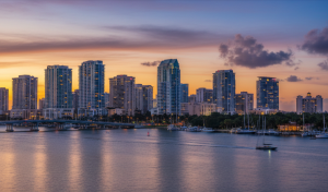 A city skyline with tall buildings at sunset, reflected on a calm body of water. Boats are docked near the shore, while the sky glows with warm orange and purple hues—perfect for an evening stroll or a case with PI Agency West Palm Beach.